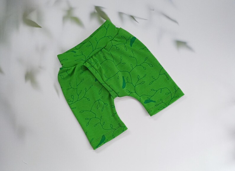 Pu&ograve; includere: Pantaloni da bambino verde brillante con un motivo di vite e uccelli verde scuro. I pantaloni hanno una vita alta e sono realizzati in tessuto morbido. Il design presenta un motivo ripetuto di viti e piccoli uccelli.