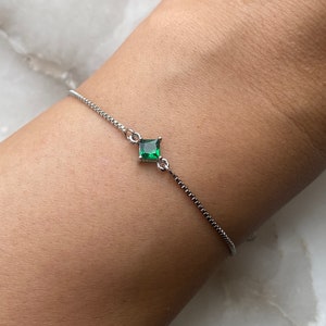 Puede incluir: Un delicado brazalete de cadena de plata con una sola piedra preciosa verde de forma cuadrada.