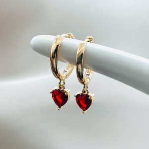 Peut inclure: Boucles d'oreilles créoles dorées avec un pendentif en forme de cœur rouge.