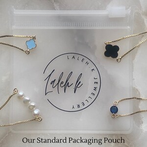 Puede incluir: Cuatro pulseras de cadena dorada con diferentes dijes en una bolsa de pl&aacute;stico transparente. Los dijes incluyen una flor azul, un tr&eacute;bol negro, una fila de perlas blancas y una piedra preciosa azul. La bolsa tiene el texto "Laleh K Jewellery" impreso en ella.