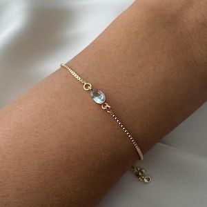 K&ouml;nnte beinhalten: Ein zartes Armband aus einer goldenen Kette mit einem Anh&auml;nger aus hellblauem Edelstein.