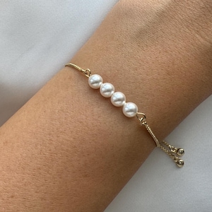 May include: A gold chain bracelet with four white pearl beads. The bracelet has an adjustable sliding clasp.
