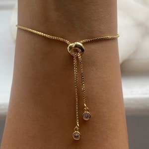 Puede incluir: Un brazalete de cadena dorada con un cierre deslizante y dos peque&ntilde;os acentos de cristal transparente.