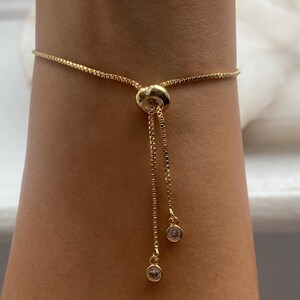 K&ouml;nnte beinhalten: Ein goldenes Kettenarmband mit einem Schiebeverschluss und zwei kleinen, klaren Kristall-Akzenten.