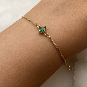 Puede incluir: Un brazalete de cadena dorada con una sola piedra preciosa verde cuadrada.