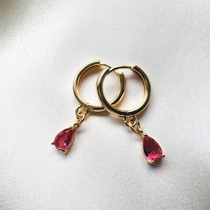 Può includere: Un paio di orecchini a cerchio dorati con pietre preziose rosa a forma di goccia che pendono.