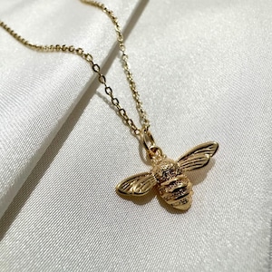 Peut inclure: Un collier en chaîne dorée avec un pendentif en forme d'abeille. L'abeille est détaillée avec des ailes texturées et un corps.
