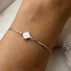 Pode incluir: Um bracelete de corrente de prata com um fecho de trevo branco e um fecho deslizante.