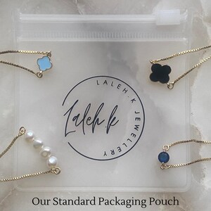 K&ouml;nnte beinhalten: Eine transparente Plastikh&uuml;lle mit dem Aufdruck "Laleh.K Jewellery". Die H&uuml;lle enth&auml;lt drei goldene Kettenarmb&auml;nder mit verschiedenen Anh&auml;ngern: ein blaues Kleeblatt, ein schwarzes Kleeblatt und eine Reihe wei&szlig;er Perlen.