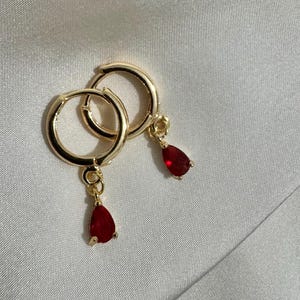 May include: A pair of gold hoop earrings with dangling red teardrop-shaped stones.