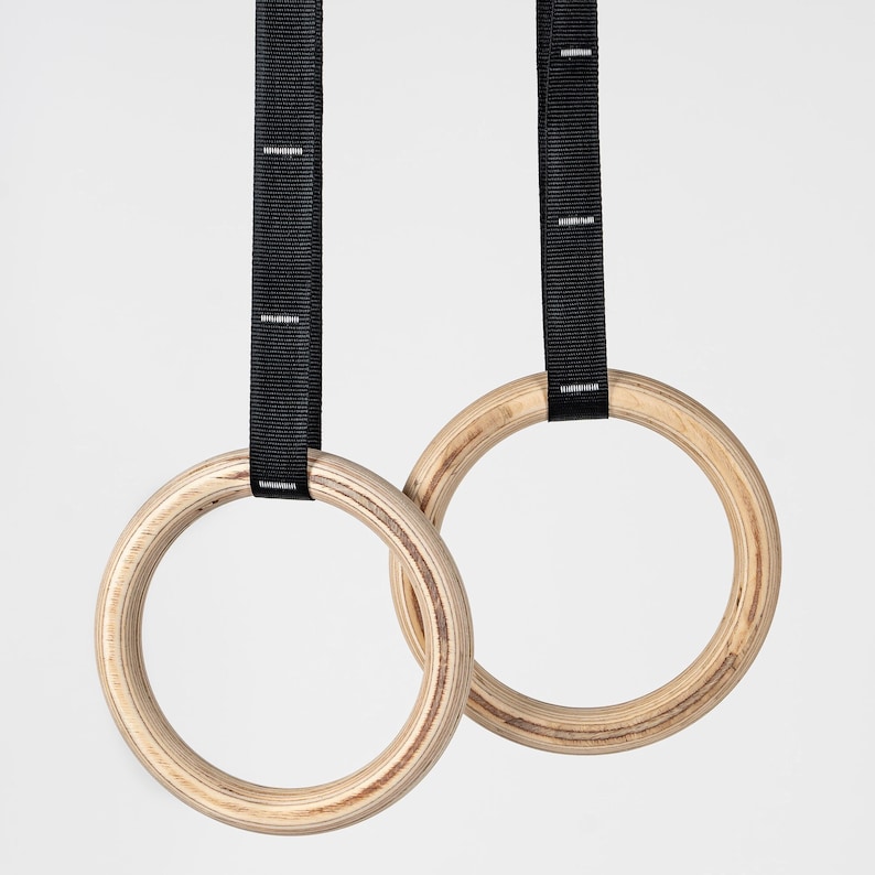May include: Two wooden gymnastic rings with black straps. The rings are made of natural wood and have a smooth finish.