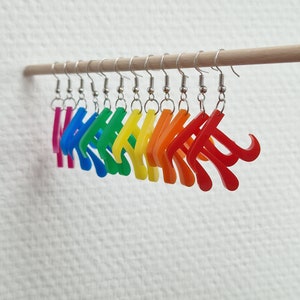 Op de afbeelding: Regenboogkleurige plastic oorbellen in de vorm van het wiskundige symbool pi die aan een houten stok hangen.