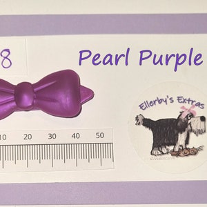 May include: A pearl purple bow, approximately 5 cm wide, is displayed on a white background with a ruler. The text "Pearl Purple" is above the bow. A sticker with a dog illustration and the text "Ellerby's Extras" is also present.
