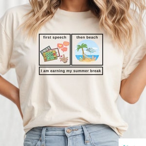 Puede incluir: Una camiseta blanca con un diseño gráfico de dos cuadrados. El cuadrado de la izquierda dice "first speech" y tiene una ilustración de una calculadora y una mano haciendo un pulgar hacia arriba. El cuadrado de la derecha dice "then beach" y tiene una ilustración de una escena de playa con una palmera, una sombrilla y una persona tumbada en una tumbona. El texto debajo de los cuadrados dice "I am earning my summer break."