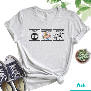 May include: A light gray t-shirt with the words "stop", "collaborate", and "listen" printed on it. Each word is in a black box with a symbol next to it. The symbol for "stop" is a red stop sign, the symbol for "collaborate" is a circle with five hands clasped together, and the symbol for "listen" is a hand cupping an ear.