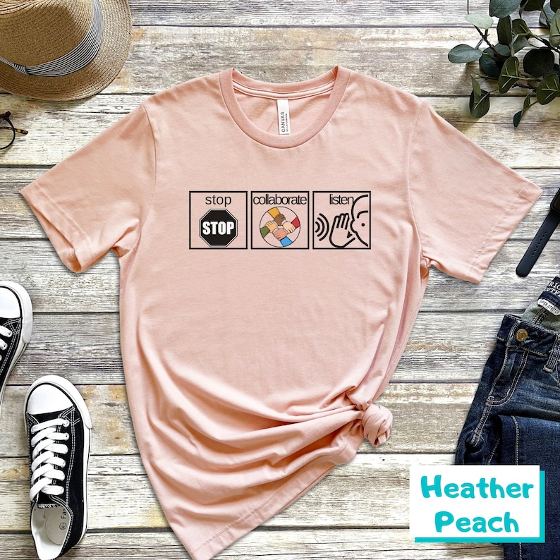 May include: A pink t-shirt with a graphic of three icons. The first icon is a stop sign with the word "STOP" inside. The second icon is a circle with five hands of different skin tones holding each other. The third icon is a hand cupping an ear with the word "listen" above it. The text "collaborate" is above the second icon. The text "stop" is above the first icon. The text "listen" is above the third icon. The t-shirt is labeled "Heather Peach".