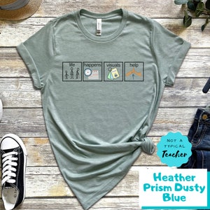 May include: A light green t-shirt with a graphic of four squares with the words "life", "happens", "visuals", and "help" and stick figure illustrations. The text "Not a Typical Teacher" is on a white circle with a blue border. The text "Heather Prism Dusty Blue" is below the circle.