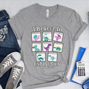 May include: Gray t-shirt with a graphic of dinosaurs and the text "I Believe In Extinction Bursts". The dinosaurs are in squares with their names below them. The dinosaurs are: Diplodocus, Brontosaurus, Pterodactyl, Triceratops, Allosaurus, Stegosaurus, Elasmosaurus, and Spinosaurus.