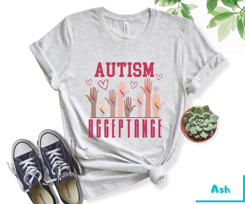 May include: A gray t-shirt with the text "AUTISM ACCEPTANCE" in red letters. The design features multiple hands with the infinity symbol in different colors.