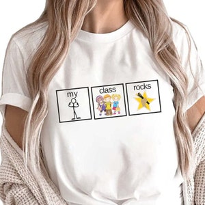 May include: White t-shirt with a graphic design that says "My class rocks". The graphic features a stick figure, a group of children, and a star with a pencil.