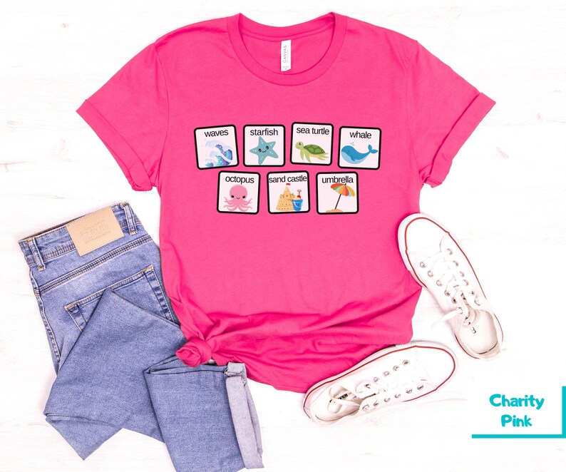 K&ouml;nnte beinhalten: Pinkes T-Shirt mit einem Grafikdruck von einem Satz Strand-Bildkarten. Die Karten zeigen Bilder von Wellen, Seesternen, Meeresschildkr&ouml;ten, Walen, Kraken, Sandburgen und Sonnenschirmen. Der Text auf den Karten lautet: "Wellen", "Seestern", "Meeresschildkr&ouml;te", "Wal", "Kraken", "Sandburg" und "Sonnenschirm".