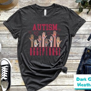 May include: Dark gray heather t-shirt with the text "AUTISM ACCEPTANCE" in red. The design features multiple hands with the autism awareness symbol in different colors.