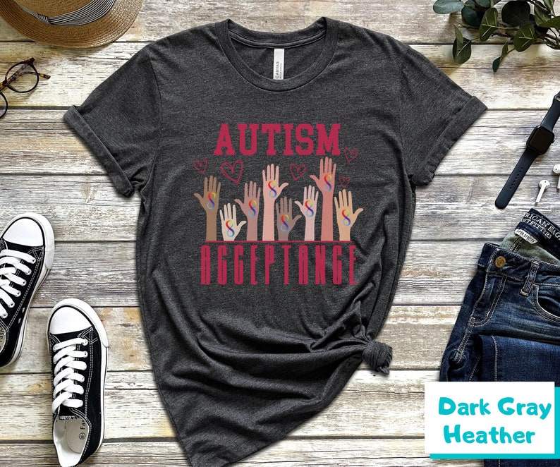 May include: Dark gray heather t-shirt with the text "AUTISM ACCEPTANCE" in red. The design features multiple hands with the autism awareness symbol in different colors.