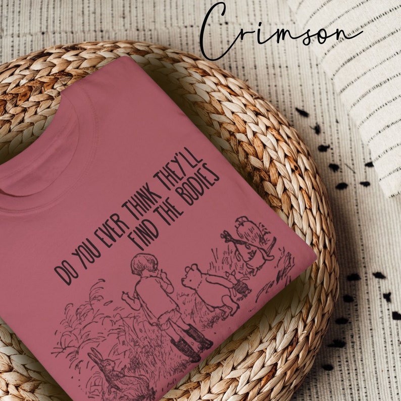 May include: A crimson t-shirt with a black graphic print of Winnie the Pooh and friends. The text on the shirt reads "Do you ever think they'll find the bodies."