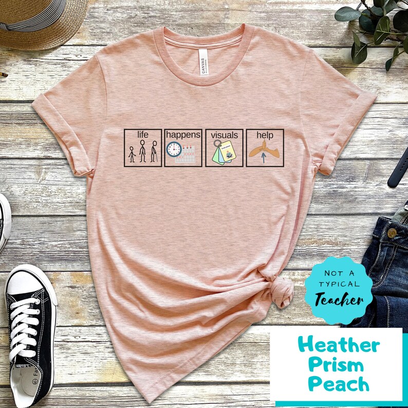May include: A pink t-shirt with a graphic of four squares. Each square has a different icon and text. The text in the squares reads "life", "happens", "visuals", and "help". The shirt also has the text "Not a Typical Teacher" and "Heather Prism Peach" printed on it.