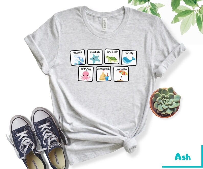 K&ouml;nnte beinhalten: Ein hellgraues T-Shirt mit einer Grafik von Strand-Icons in Quadraten. Die Icons beinhalten Wellen, einen Seestern, eine Meeresschildkr&ouml;te, einen Wal, einen Oktopus, eine Sandburg und einen Regenschirm. Der Text "waves", "starfish", "sea turtle", "whale", "octopus", "sand castle", und "umbrella" ist unter jedem Icon gedruckt.