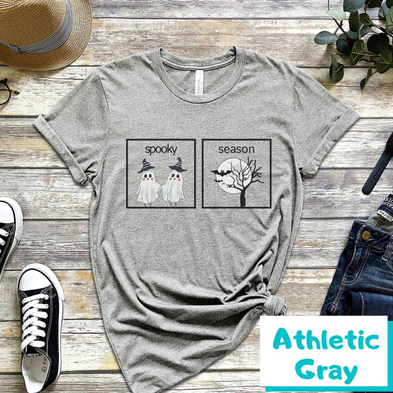 K&ouml;nnte beinhalten: Ein graues T-Shirt mit einem Aufdruck von zwei Geistern mit Hexenh&uuml;ten und dem Text "spooky" und einem Baum mit Flederm&auml;usen und dem Text "season".