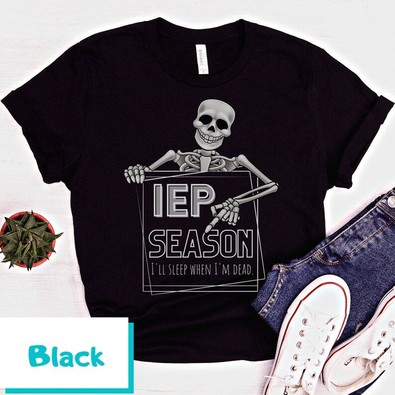 May include: Black t-shirt featuring a skeleton holding a sign that reads "IEP SEASON" with the text "I'll sleep when I'm dead." The design is in gray and white. The shirt is paired with blue jeans and white sneakers.