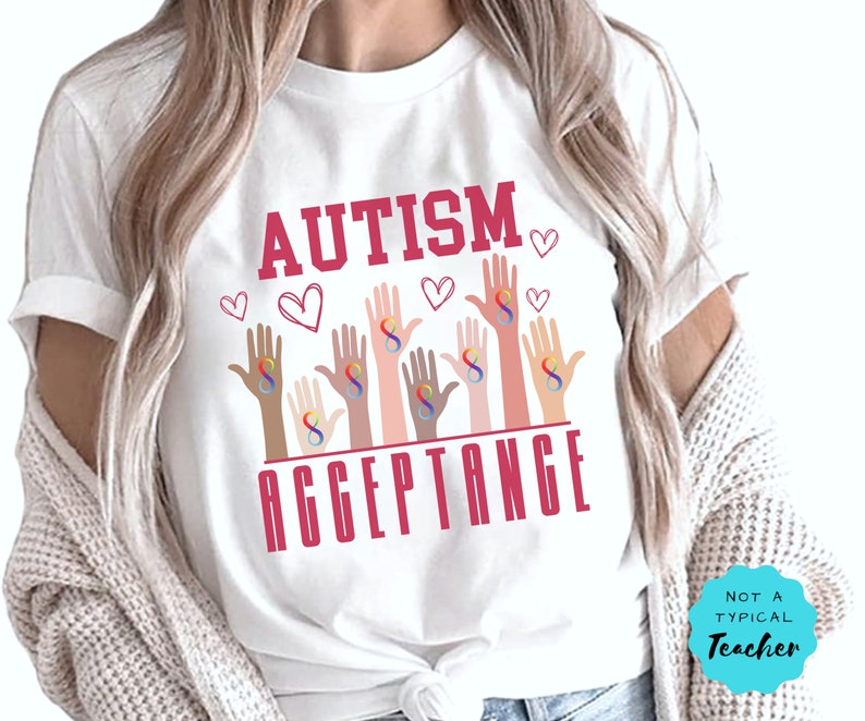 May include: White t-shirt with the text "AUTISM ACCEPTANCE" in pink lettering. The design features multiple hands with rainbow infinity symbols, representing autism awareness.