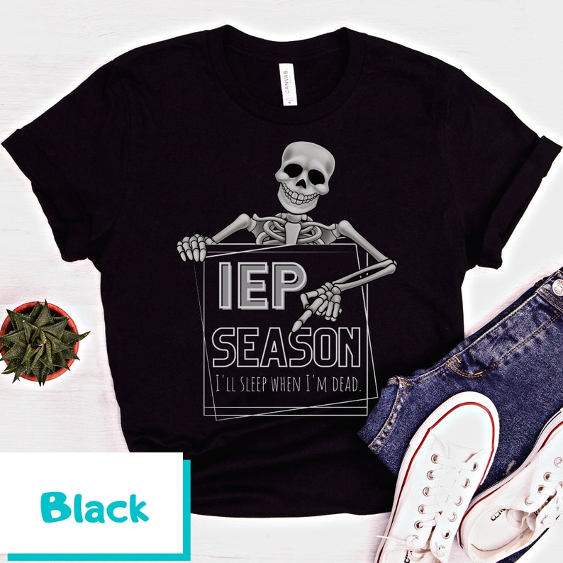May include: Black t-shirt featuring a skeleton holding a sign that reads "IEP SEASON" with the text "I'll sleep when I'm dead." The design is in gray and white. The shirt is paired with blue jeans and white sneakers.
