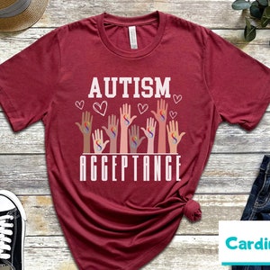 May include: Red t-shirt with the text "AUTISM ACCEPTANCE" in white letters. The design features multiple hands with infinity symbols in rainbow colors.