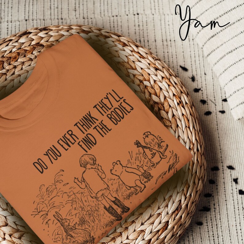 May include: A brown t-shirt with the text "Do you ever think they'll find the bodies" printed on it. The shirt features a black and white illustration of Winnie the Pooh and his friends in the Hundred Acre Wood.
