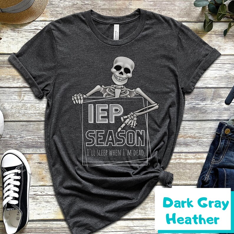May include: Dark gray heather t-shirt with a skeleton graphic holding a sign that reads "IEP SEASON" and "I'll sleep when I'm dead". The shirt is a dark gray color and has a classic crew neck.