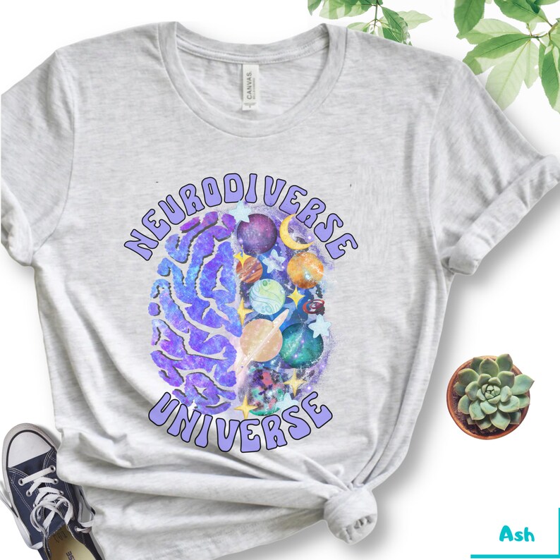 Może przedstawiać: Szara koszulka z nadrukiem fioletowego m&oacute;zgu i tekstem "Neurodiverse Universe" w fioletowym, retro stylu.