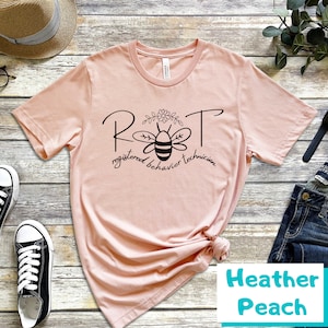 May include: A pink t-shirt with a black bee graphic and the text "RBT registered behavior technician".