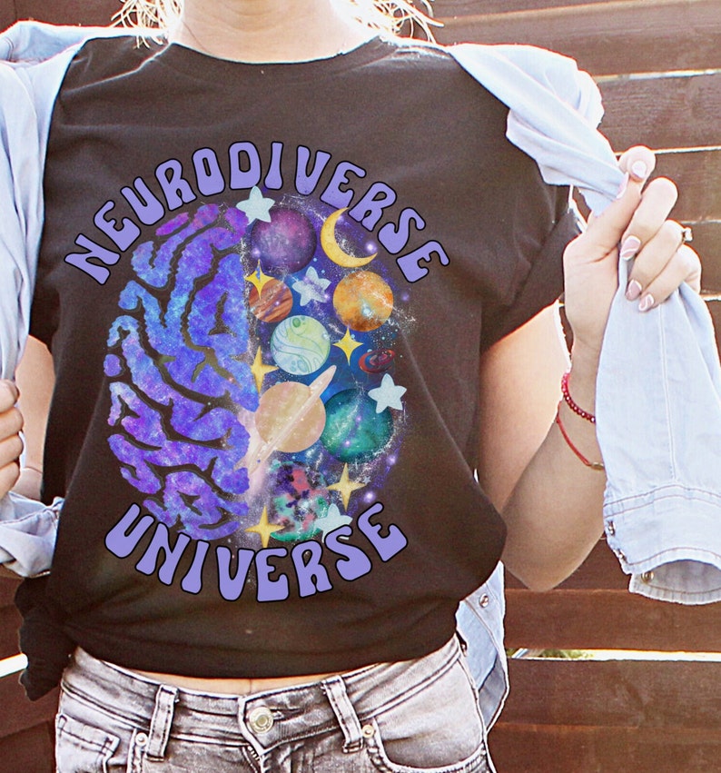 Może przedstawiać: Czarny T-shirt z grafiką m&oacute;zgu w kolorze fioletowym i niebieskim, z galaktyką i planetami w środku. Tekst "Neurodiverse Universe" jest napisany fioletowym kolorem wok&oacute;ł grafiki m&oacute;zgu.