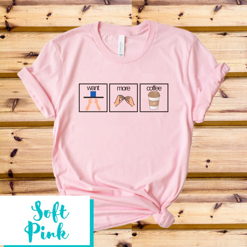 May include: A pink t-shirt with a graphic of three boxes. The first box says "want" and shows a hand reaching for a blue cup. The second box says "more" and shows a hand making the sign for "more". The third box says "coffee" and shows a cup of coffee.