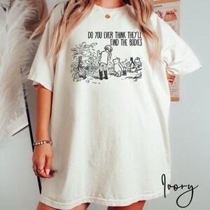 May include: An oversized white t-shirt featuring a black graphic print of Winnie the Pooh and Piglet. The text on the shirt reads "Do you ever think they'll find the bodies".