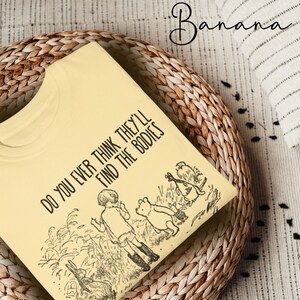 May include: A yellow t-shirt with a black graphic print of Winnie the Pooh and friends. The text on the shirt reads "Do you ever think they'll find the bodies."