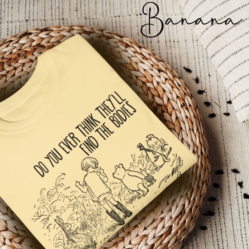 May include: A yellow t-shirt with a black graphic print of Winnie the Pooh and friends. The text on the shirt reads "Do you ever think they'll find the bodies."