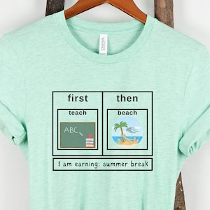 May include: A light green t-shirt with a graphic of a chart that says "first: teach" with a chalkboard and books and "then: beach" with a beach scene. The text below the chart says "I am earning: summer break".