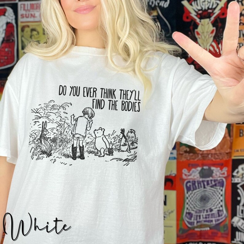 May include: White t-shirt featuring a black and white illustration of Winnie the Pooh and his friends. The text "Do you ever think they'll find the bodies" is printed on the shirt.