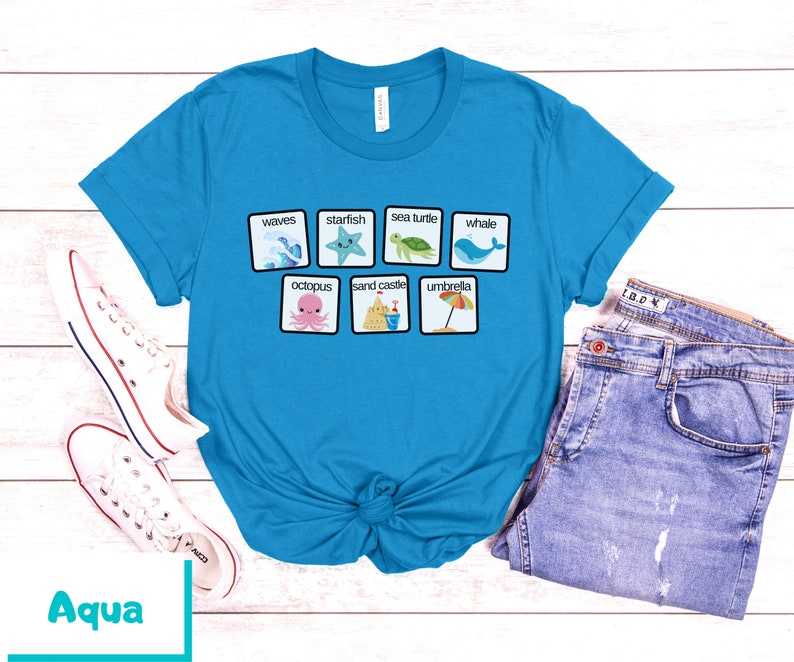 K&ouml;nnte beinhalten: Ein t&uuml;rkisfarbenes T-Shirt mit einer wei&szlig;en Grafik von Strandmotiven und W&ouml;rtern, darunter "Wellen", "Seestern", "Meeresschildkr&ouml;te", "Wal", "Kraken", "Sandburg" und "Sonnenschirm".
