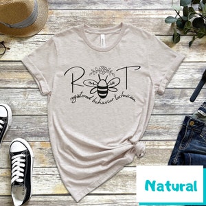 May include: A light beige t-shirt with a black bee graphic and the text "RBT registered behavior technician".
