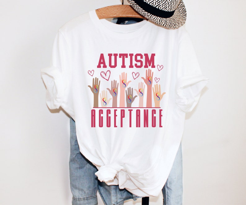 May include: White t-shirt with the words "AUTISM ACCEPTANCE" in red lettering. The design features multiple hands of different skin tones, each with a rainbow infinity symbol.