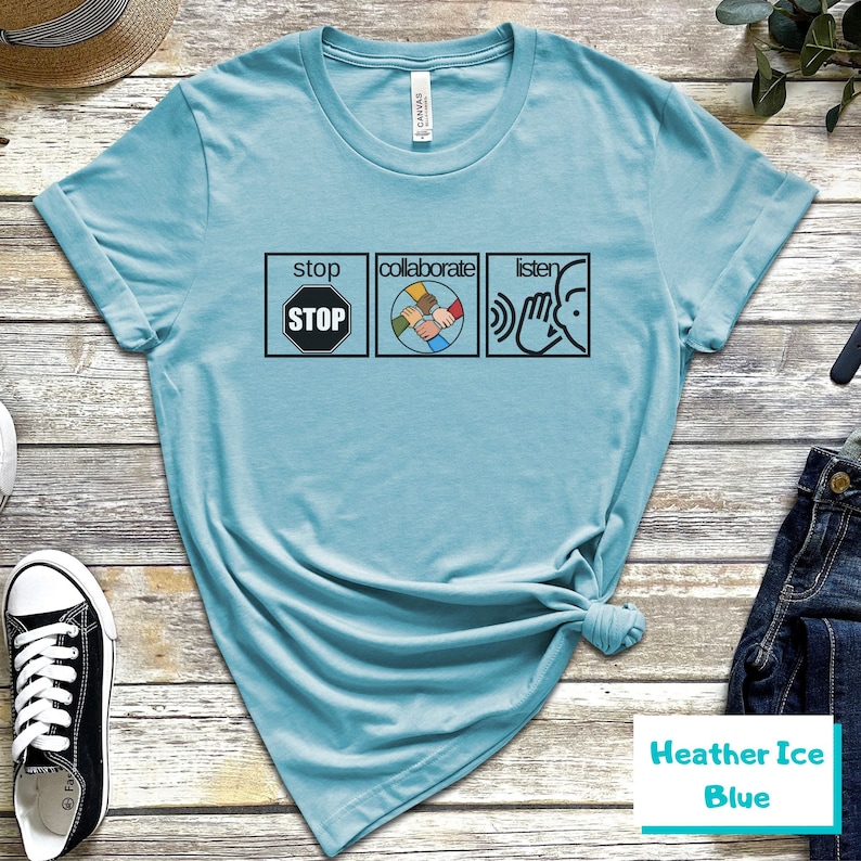 May include: A light blue t-shirt with the words "stop", "collaborate", and "listen" printed on it. Each word is in a separate box with a symbol next to it. The symbol for "stop" is a red octagon with the word "STOP" in white letters. The symbol for "collaborate" is a circle with four hands of different colors holding each other. The symbol for "listen" is a hand cupping an ear.